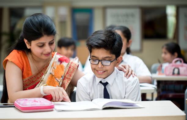 Teacher helping schoolboy to write in book at classroom